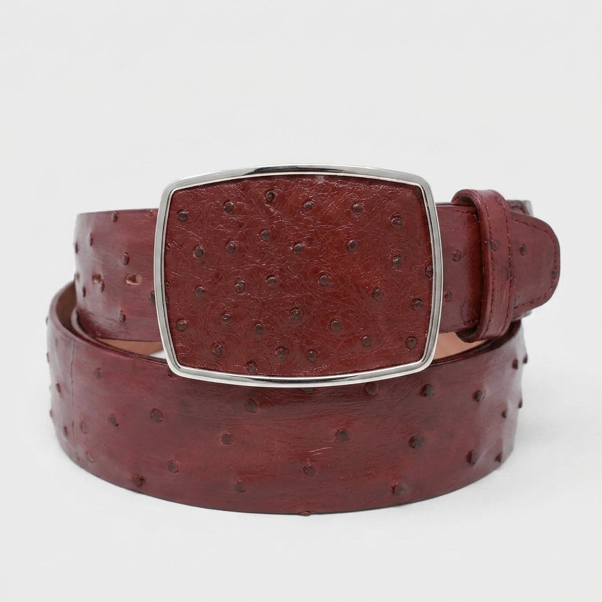Los Altos men's burgundy reddish-brown ostrich leather belt with a silver-tone rectangular buckle, coiled on a light gray background.