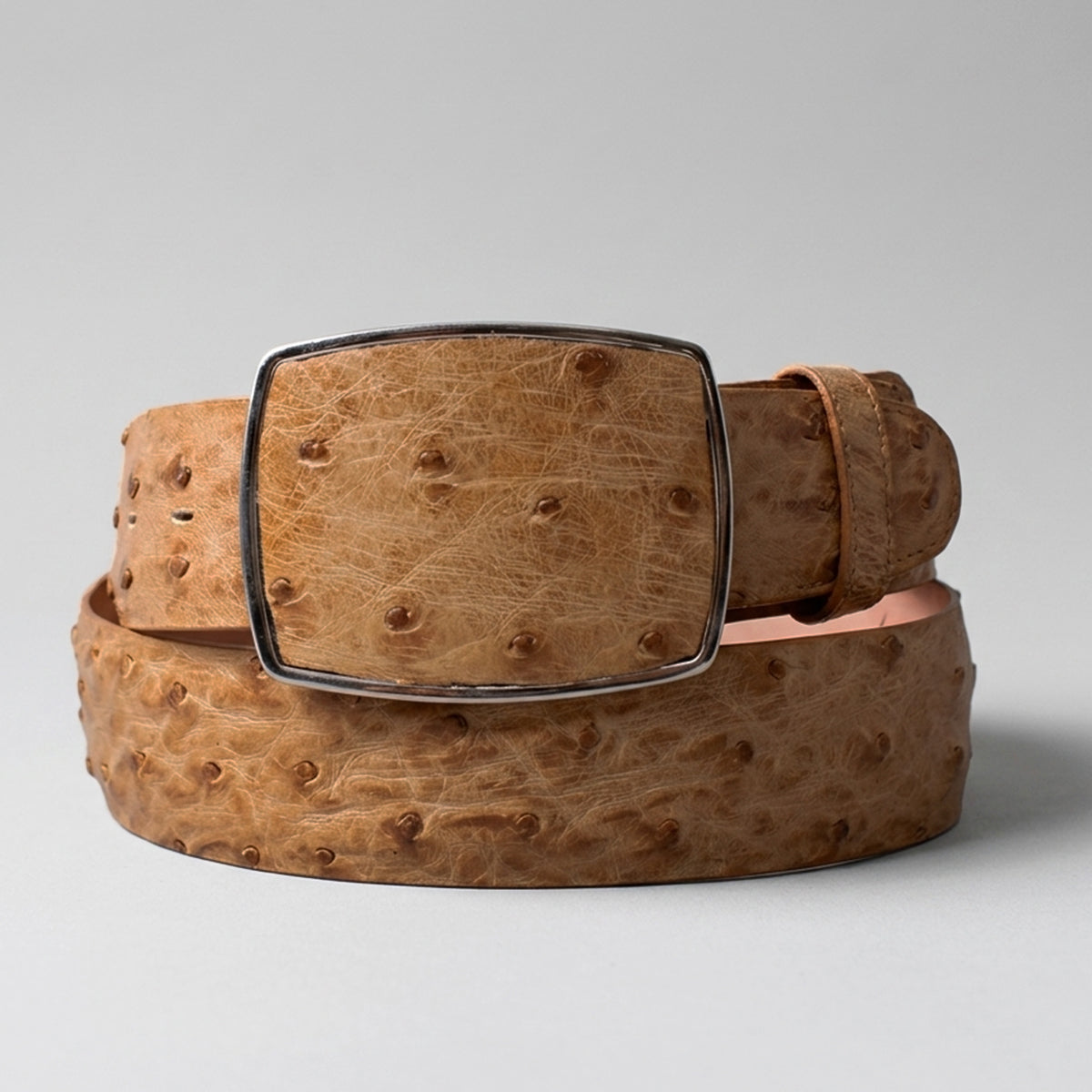 Los Altos amber tan ostrich leather belt with a silver-tone rectangular buckle, coiled on a light gray background.