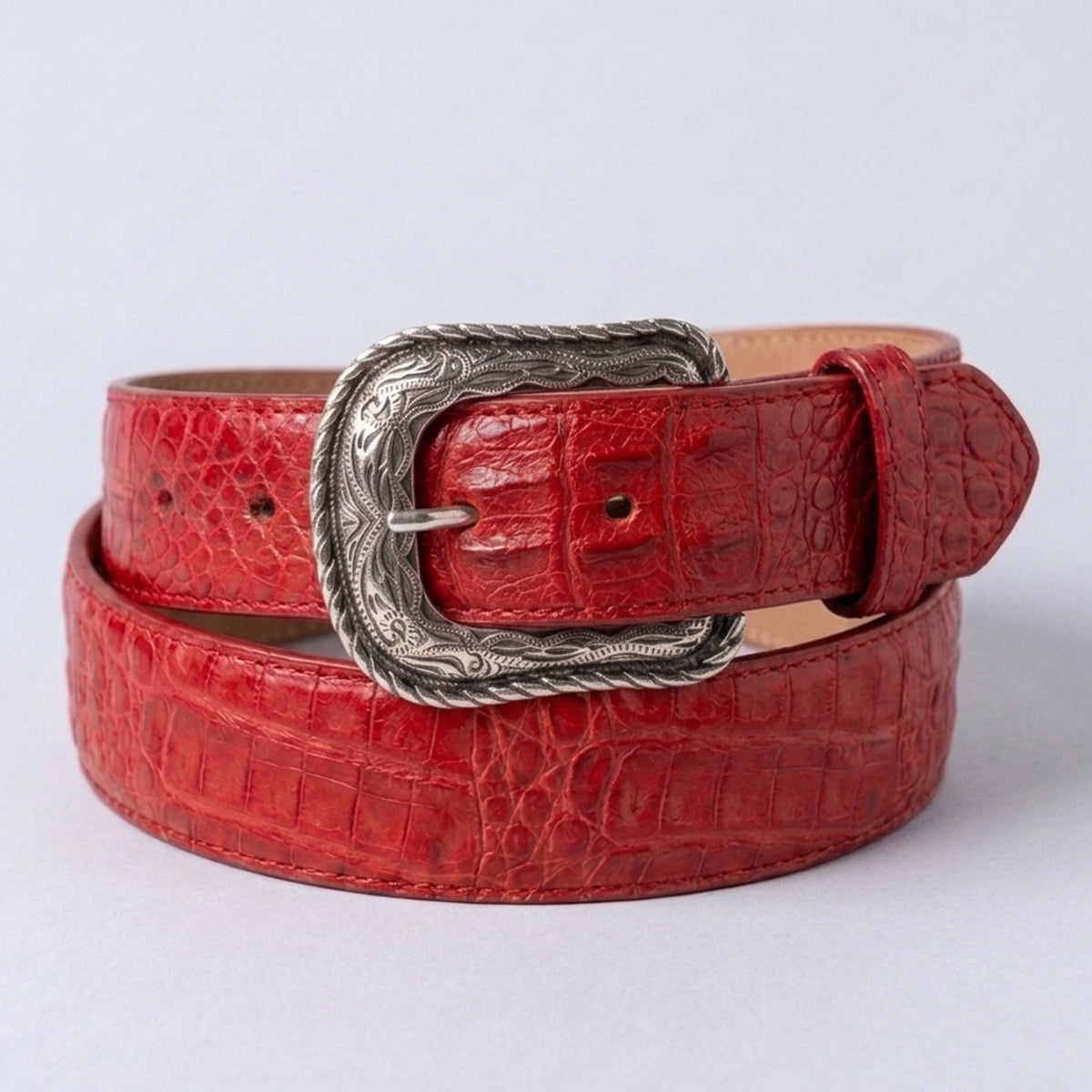 Los Altos men's red crocodile leather belt with a silver-toned western-style engraved buckle, coiled on a light gray background.