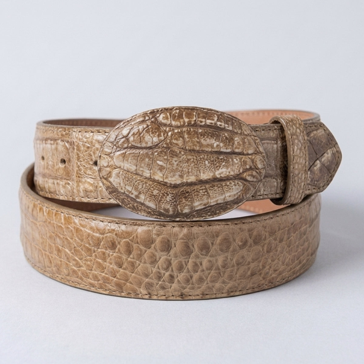 Los Altos men's Sahara stone tan crocodile leather belt with a matching textured buckle, coiled on a light gray background.