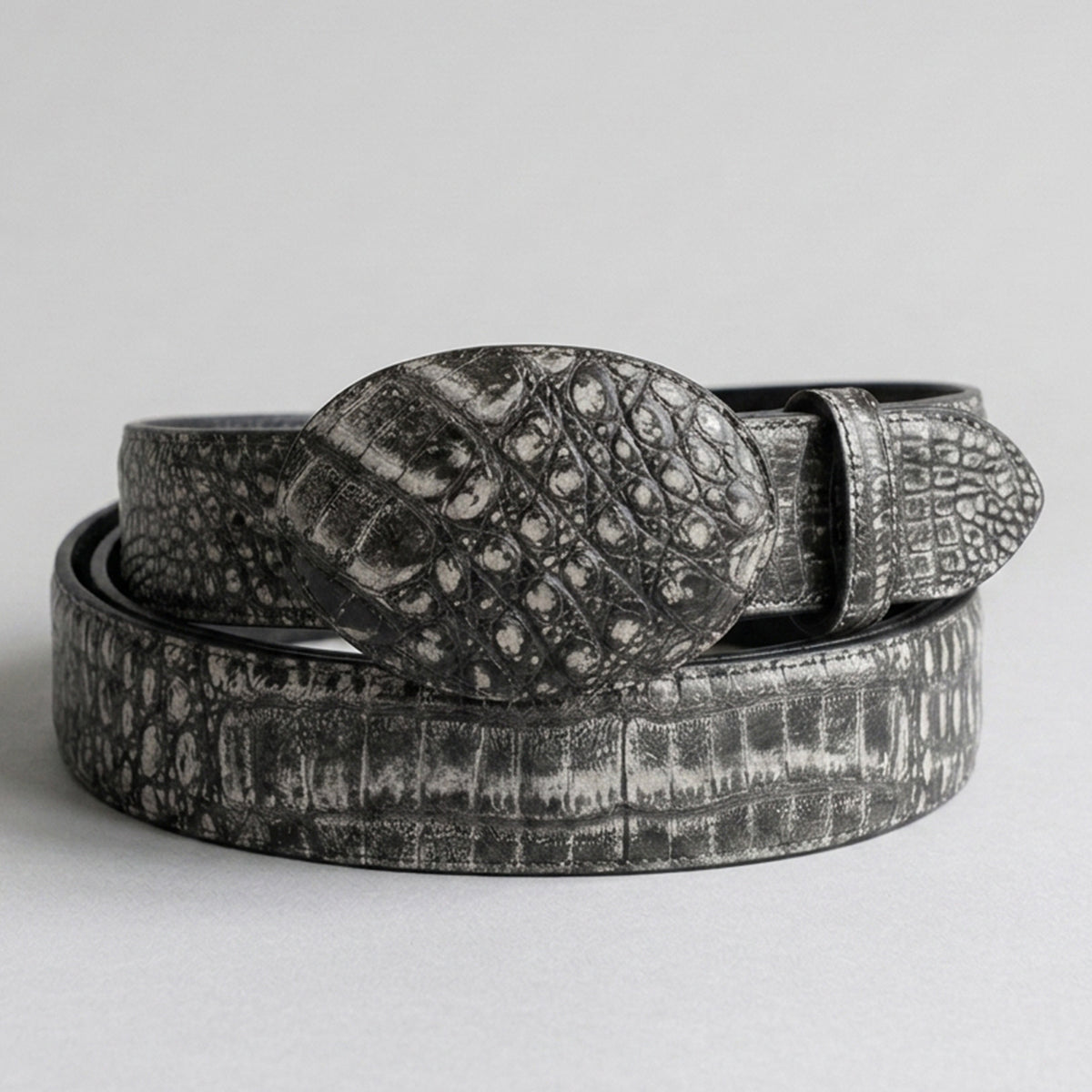 Los Altos men's caiman belly leather belt in black and gray, coiled on a light gray background.