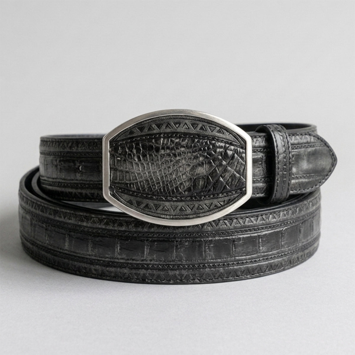 Los Altos men's faded gray genuine caiman belly leather belt showing distressed gray-black scales, laser-stitched geometric borders, and a matching clipped-corner inlay buckle.