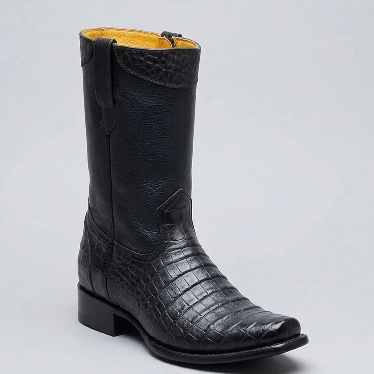 A black leather cowboy boot with a crocodile-embossed texture on the lower shafts and toes, featuring a low block heel and a light tan interior lining, shown against a neutral gray background.