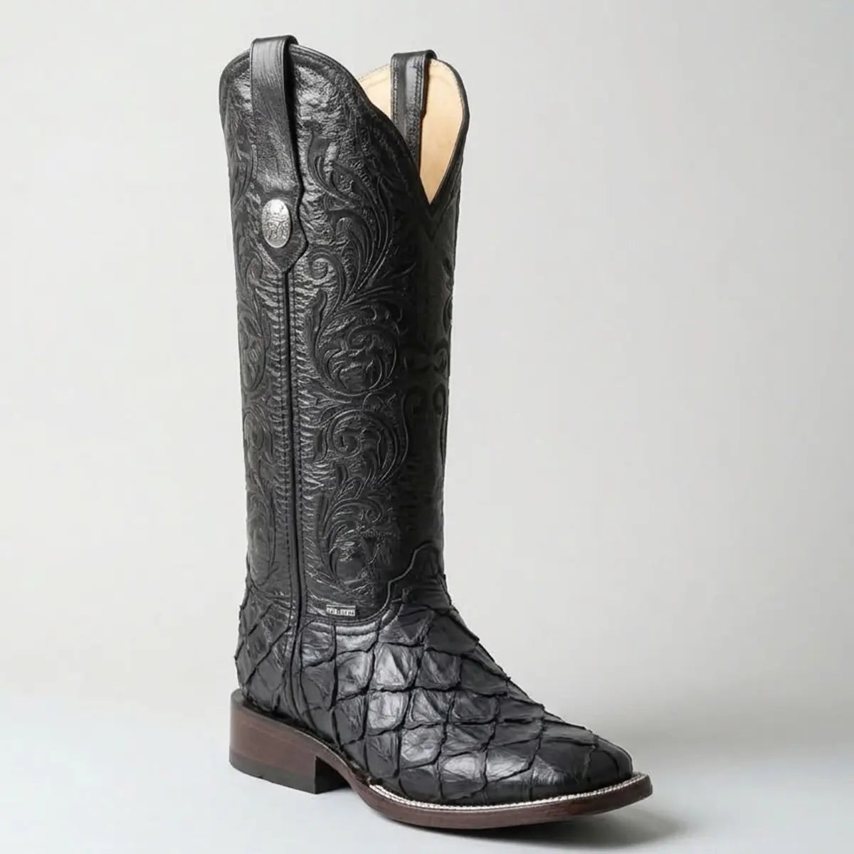 Single black Doble R women's cowgirl boot in a studio setting, featuring a genuine pirarucu fish scale vamp, a square toe, and a tall black leather shaft with tonal floral embroidery and a silver concho.