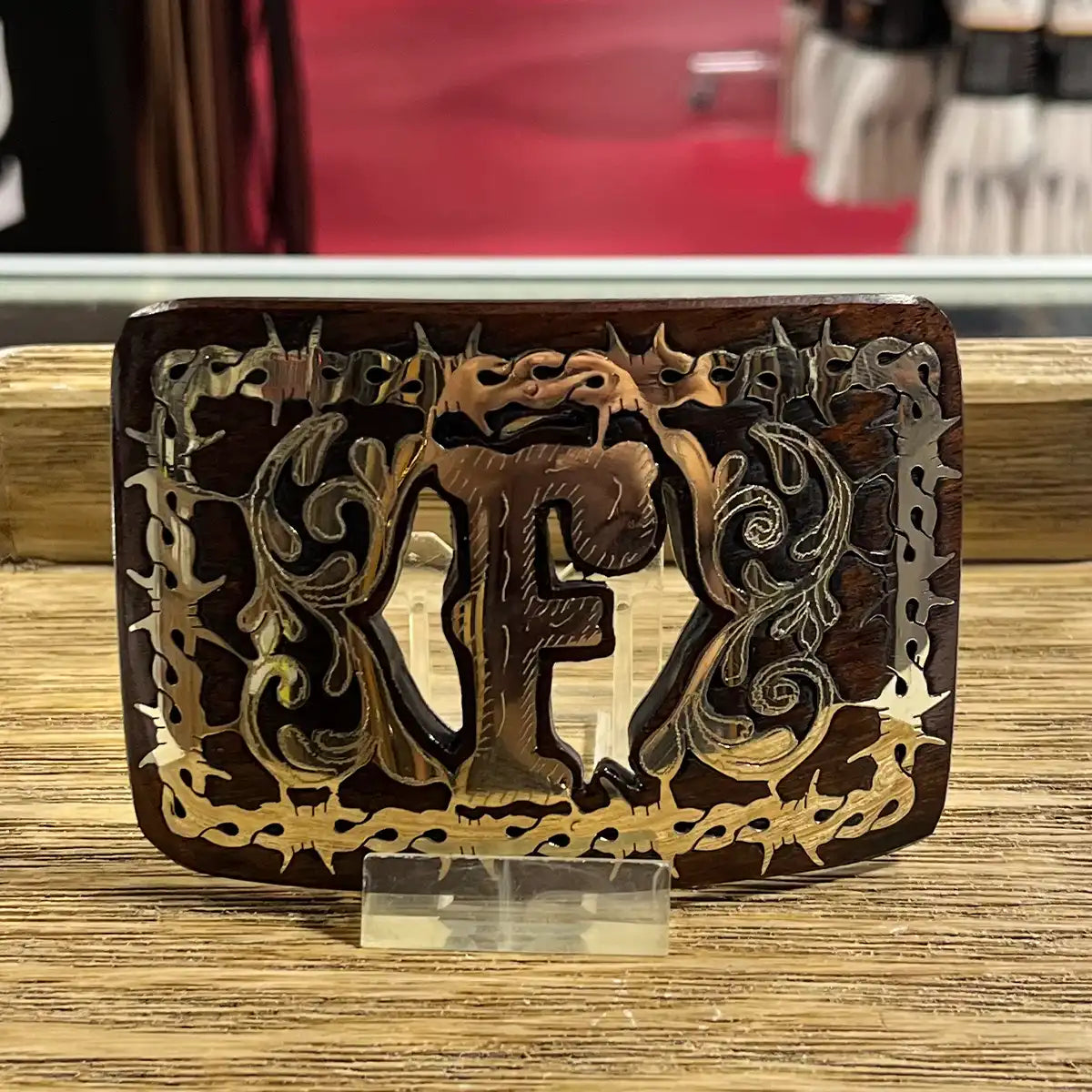 In-store counter display view of the handcrafted mesquite wood belt buckle showing the Monogram F inlay on an acrylic stand.