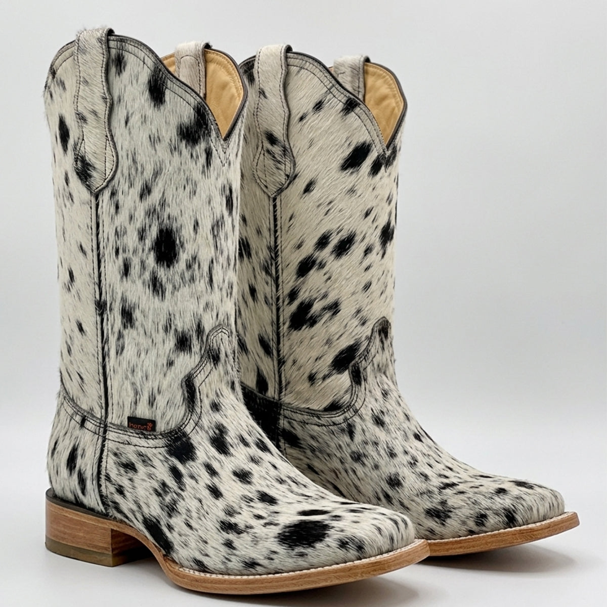 A pair of Hooch women's cowgirl boots featuring a black and white speckled hair-on hide upper, a wide square toe, and a stacked leather walking heel.