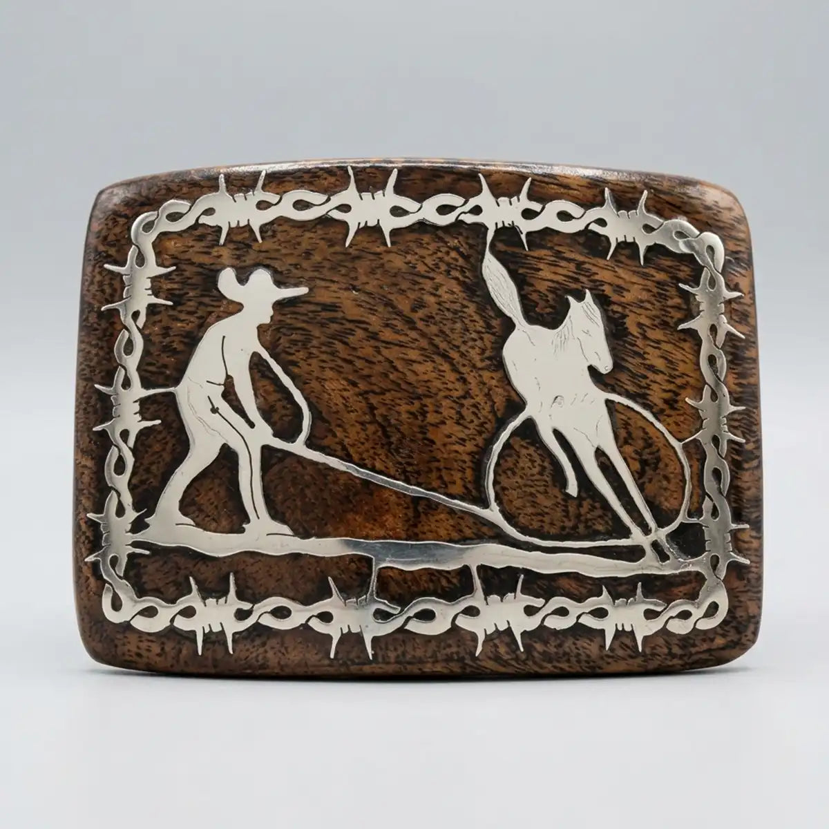 Studio view of the handcrafted mesquite wood belt buckle with metal Manganas a Pie charro scene inlay and barbed wire frame.