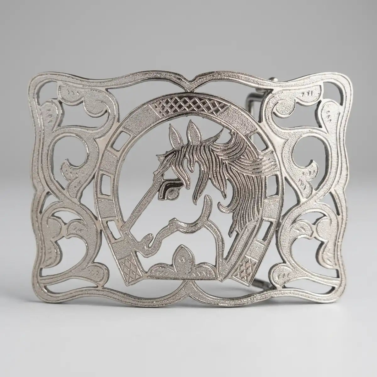 A silver-toned metal belt buckle featuring an ornate filigree design with a central horse head motif, photographed on a neutral light gray background.