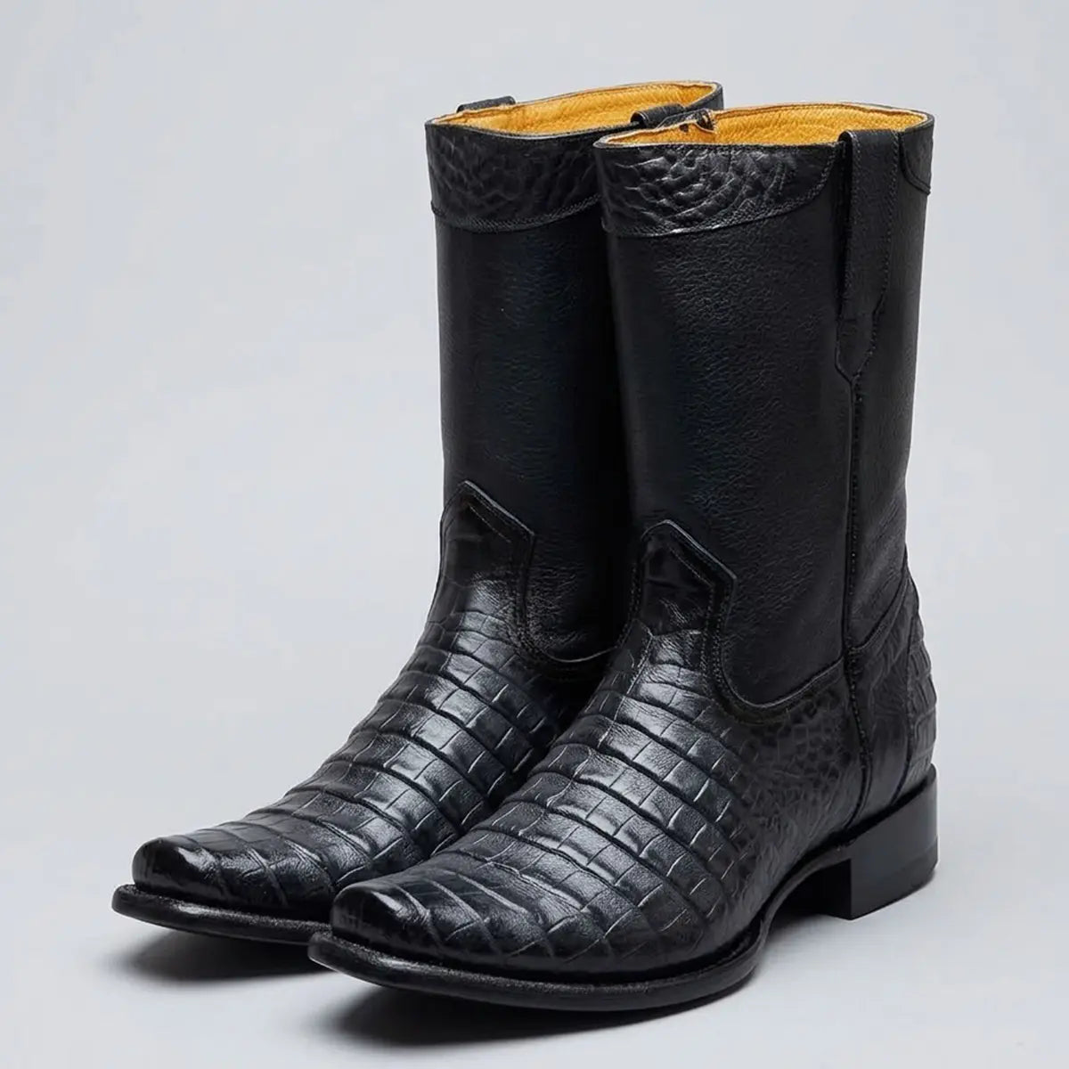 A pair of black leather cowboy boots with a crocodile-embossed texture on the lower shafts and toes, featuring a low block heel and a light tan interior lining, shown against a neutral gray background.