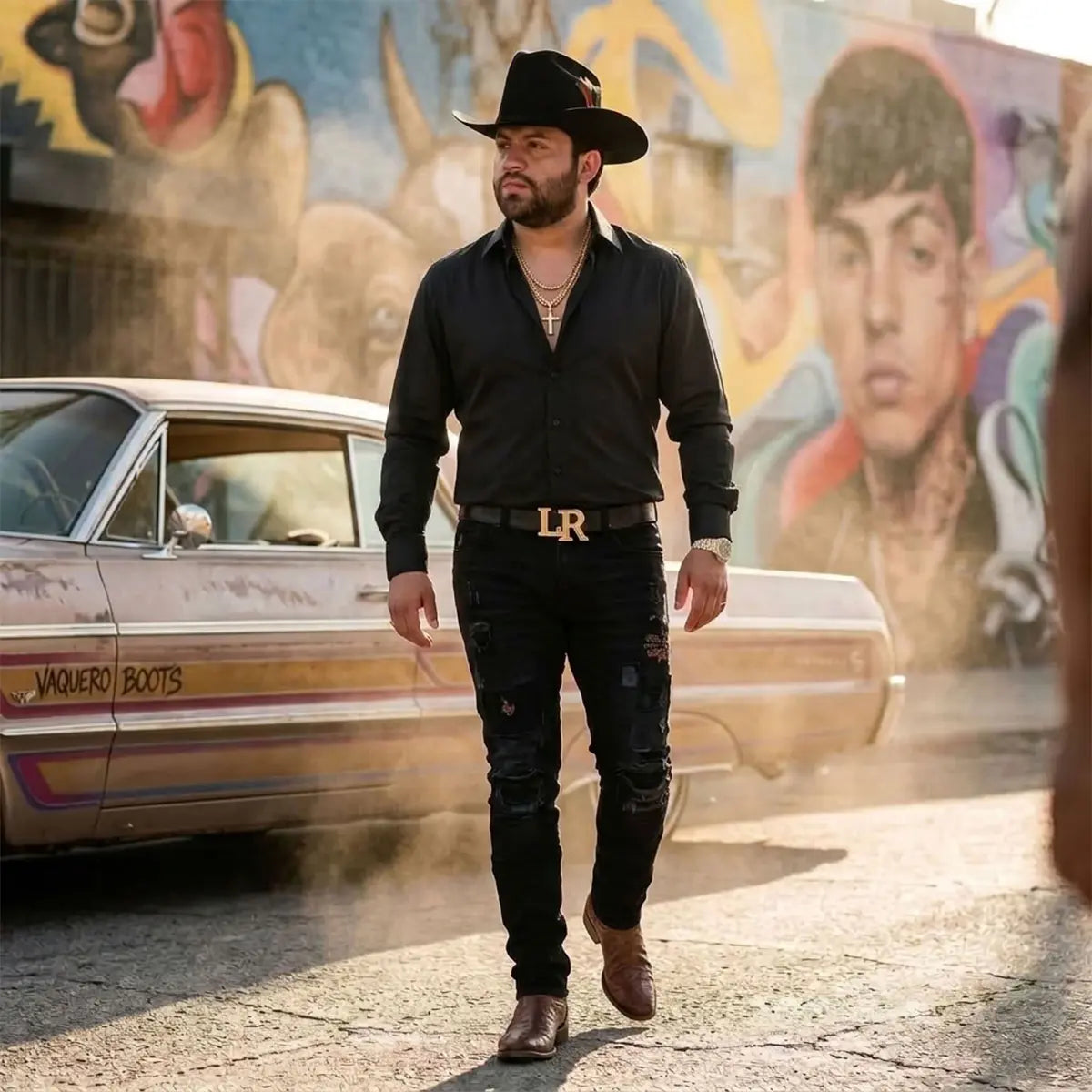 Full-length street lifestyle photo of Regional Mexican artist Luis R. Conriquez wearing his official black tejana hat, black shirt, LR belt buckle, black jeans, and brown leather boots.
