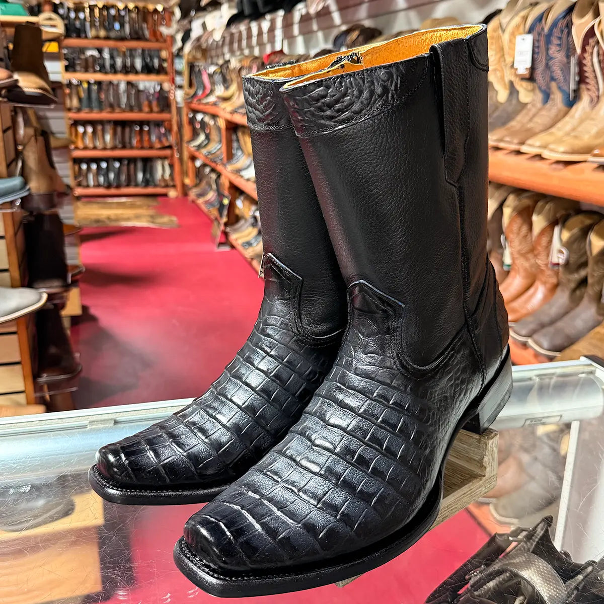Retail display view of the La Sierra Men's Grain Black caiman print boots showing the semi square toe, short 8" shaft, side zipper, and leather outsole.