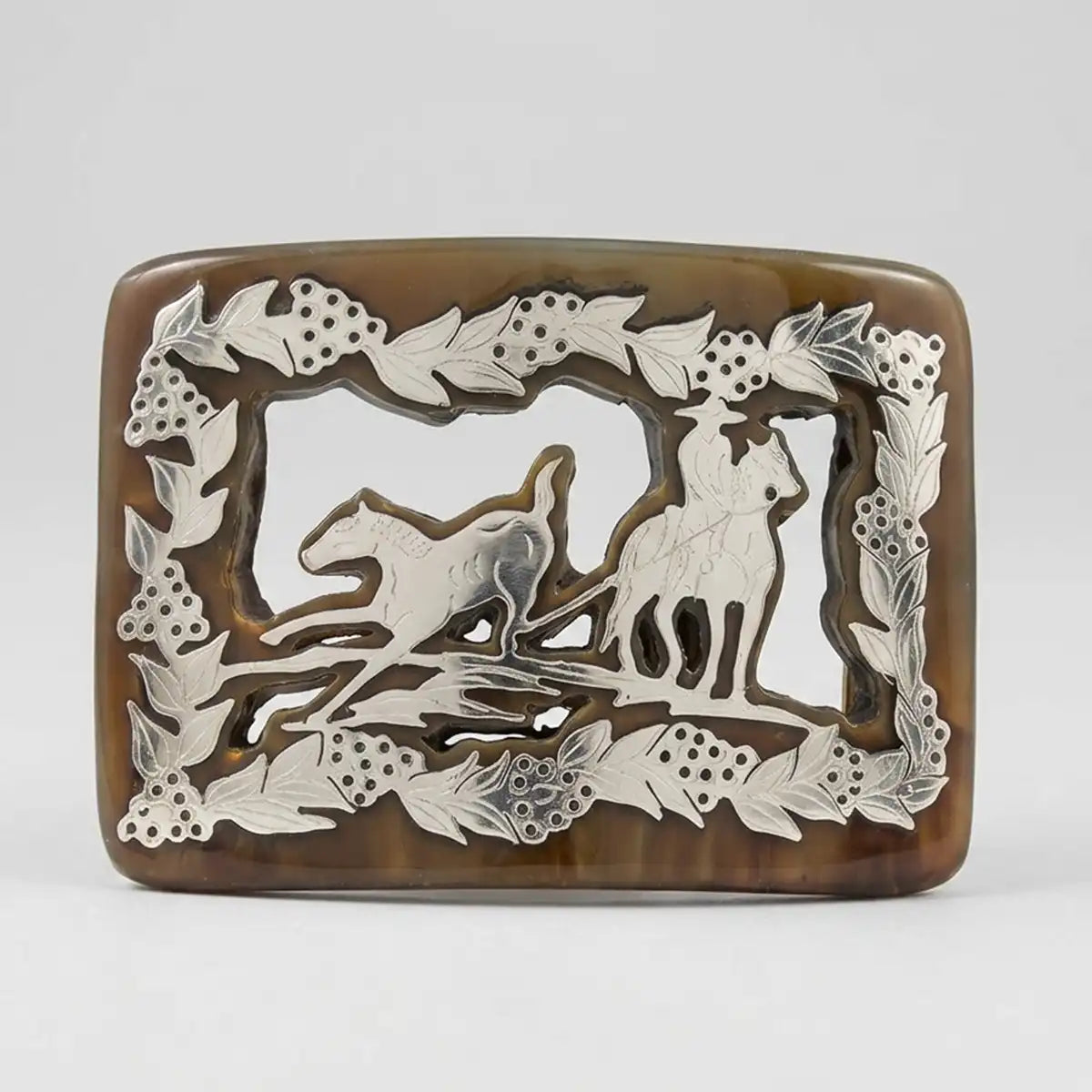 Studio view of the genuine bull horn belt buckle with metal Piales en Lienzo charro scene inlay and leaf garland border.