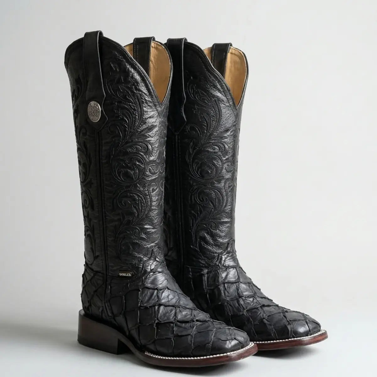 Pair of women's black Doble R pirarucu western boots against a light background, showcasing the large fish scale texture on the foot, deep V-cut collar, and dark block heels.