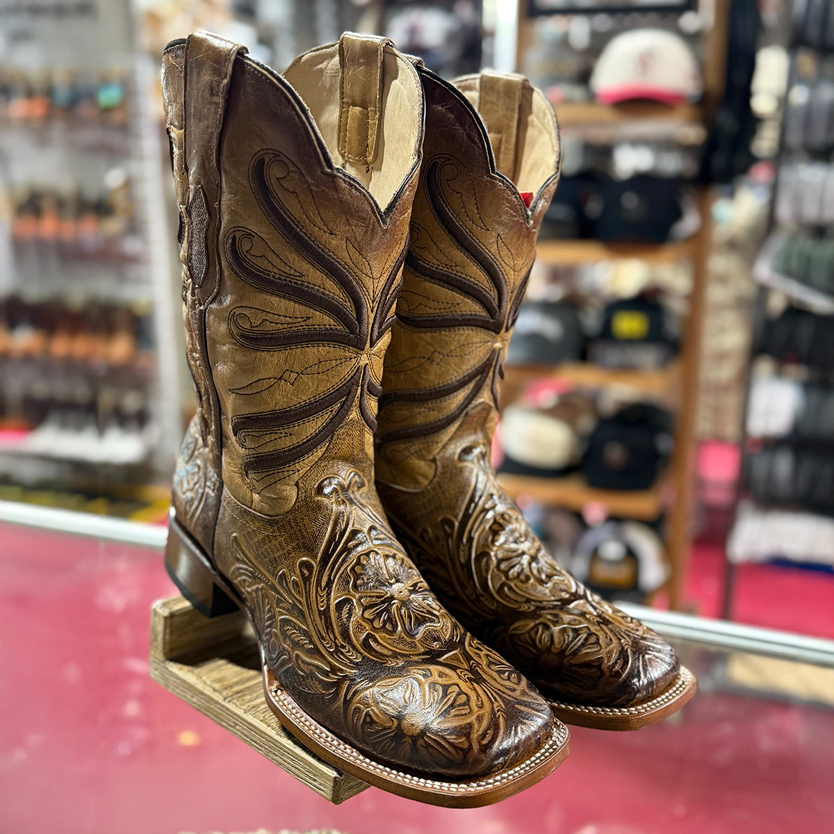 Pair of Quincy men's brown square toe cowboy boots with intricate tooled designs on a display stand in a western store.