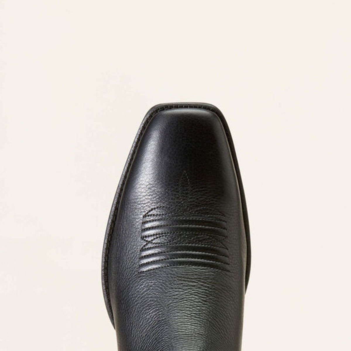Close-up of a black square toe on a beige background.
