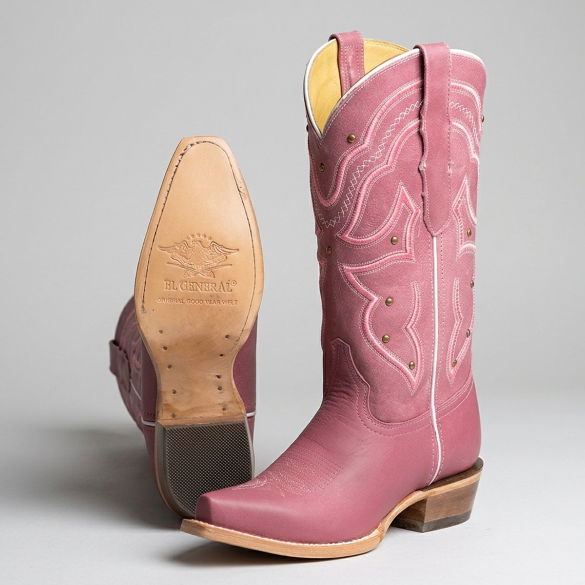 Pink cowgirl boot with a visible leather sole on a gray background.