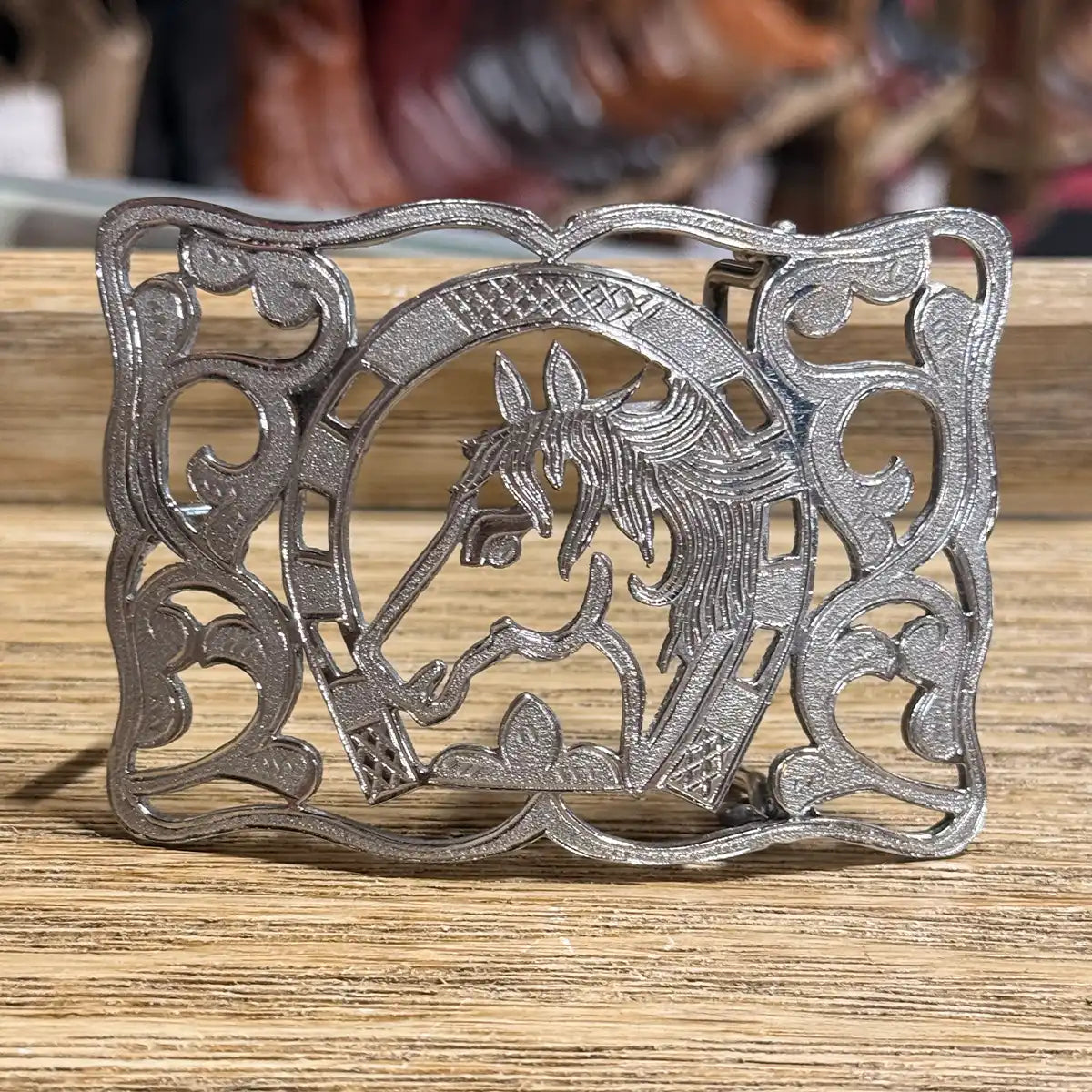 Stainless steel cutout Western belt buckle featuring a detailed horse profile framed in a horseshoe with intricate filigree scrollwork.