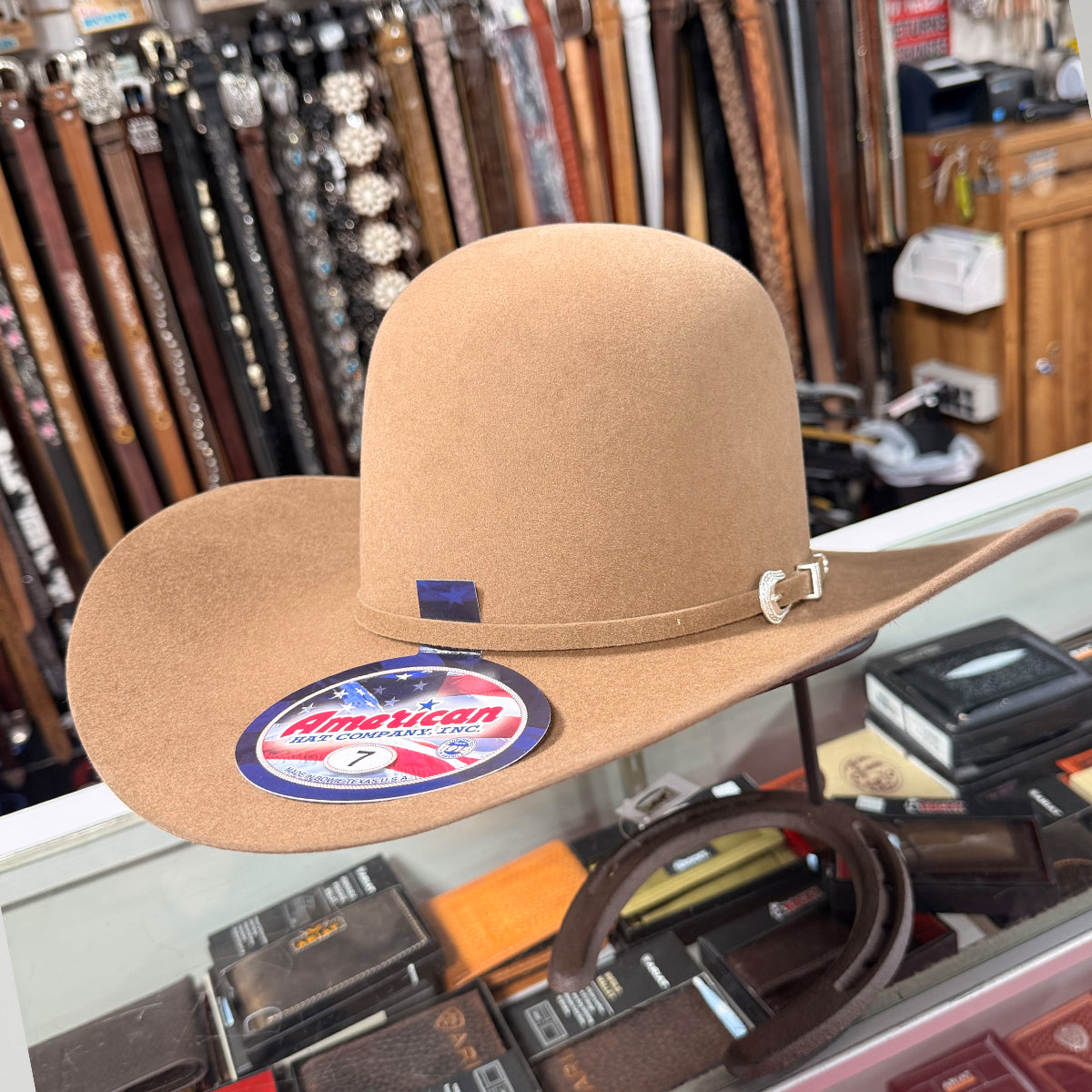 American Hat brown cowboy hat with a visible brand logo on a glass surface with various items in the background.