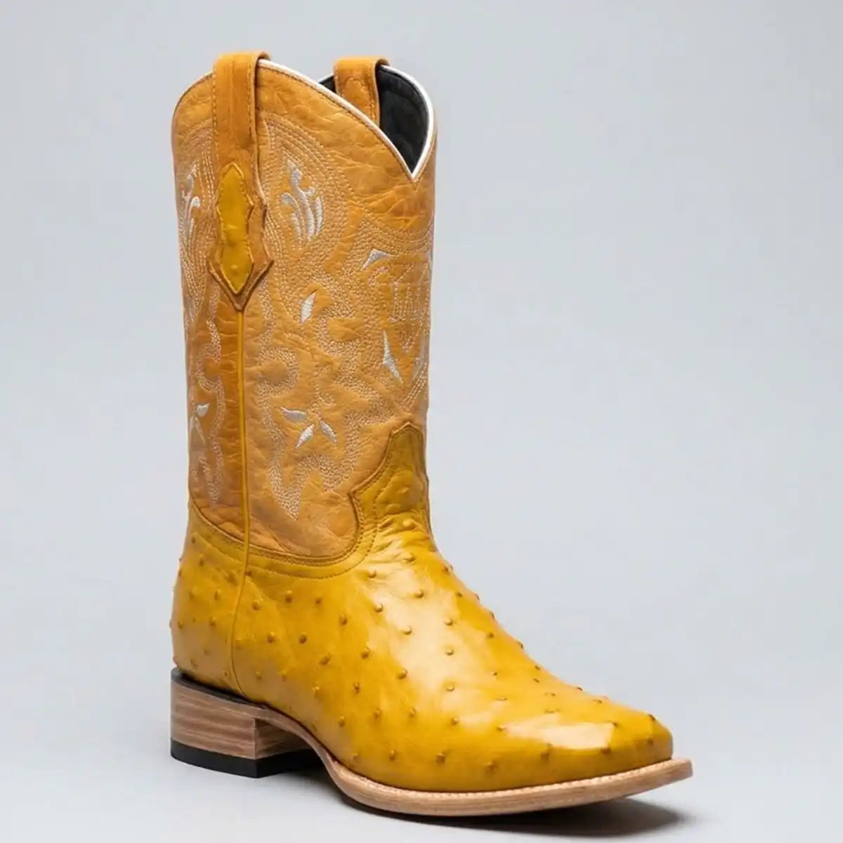 A yellow ostrich print square toe cowboy boot with white western embroidery on the shafts, shown against a neutral gray background.