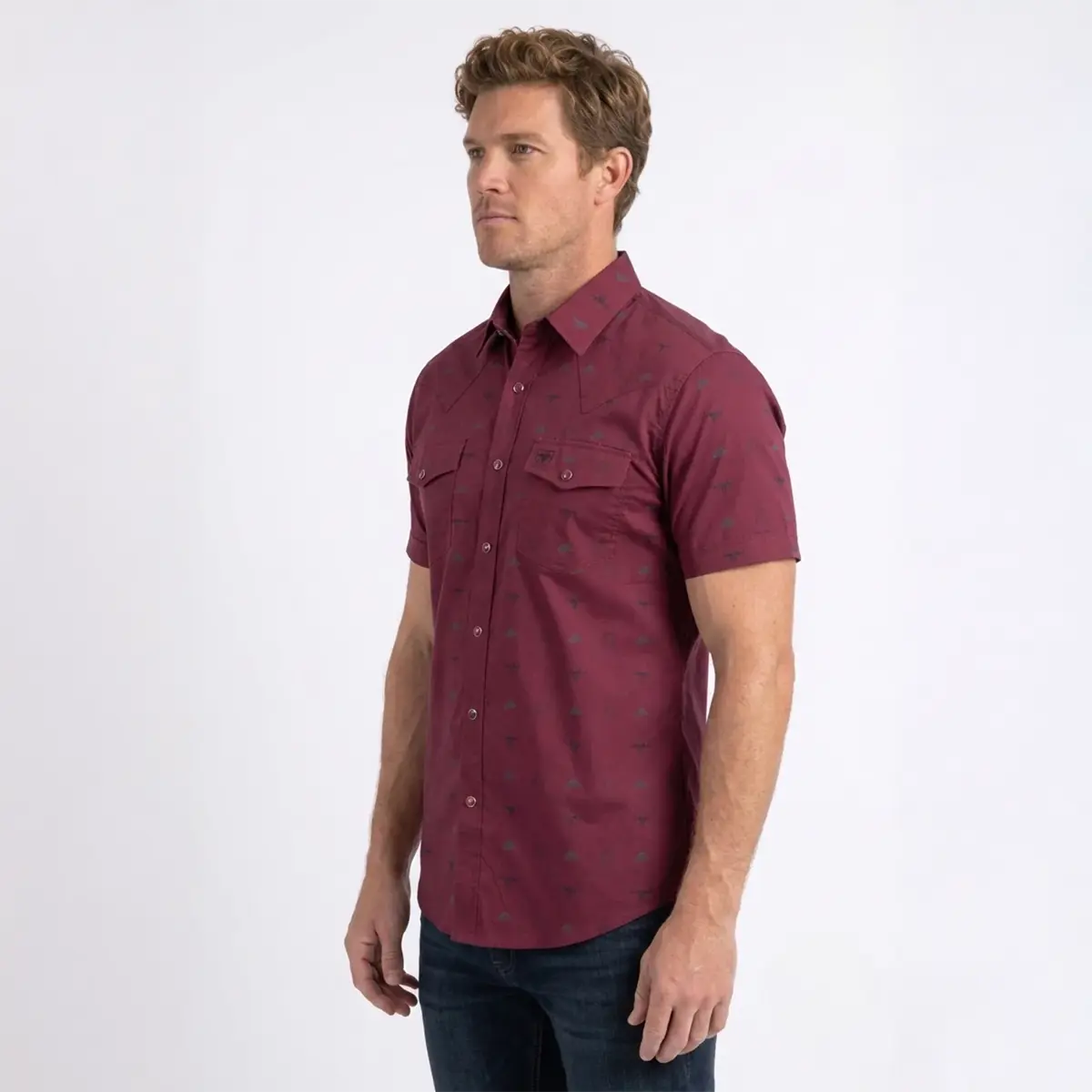 Three-quarter studio view of a male model wearing the Platini Men's burgundy longhorn icon short sleeve snap shirt paired with dark denim jeans.