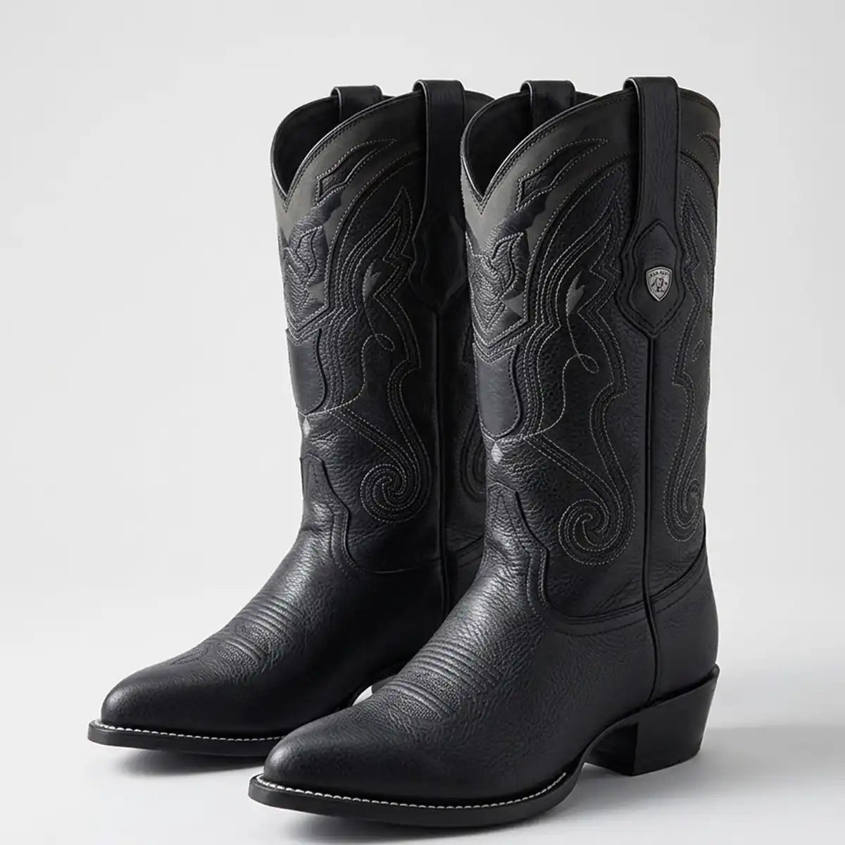 A pair of black leather cowboy boots with decorative embossed western stitching, shown on a light gray studio background.