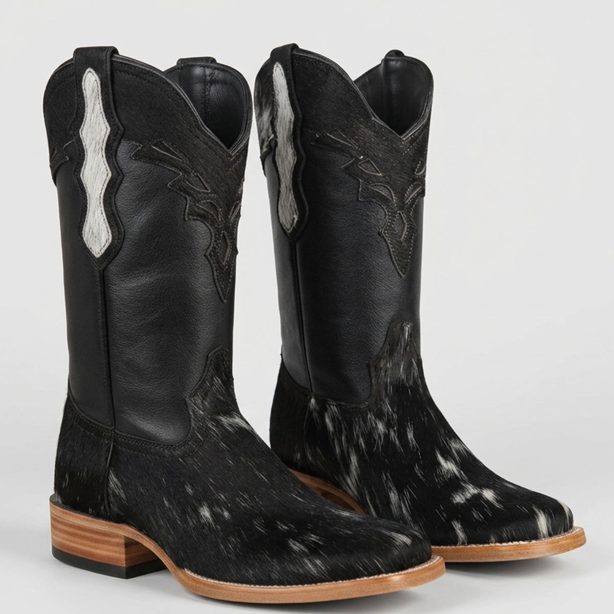 Women's black leather square toe cowboy boots with a genuine black and white cowhide hair-on-hide vamp and an inlay design on the shaft.