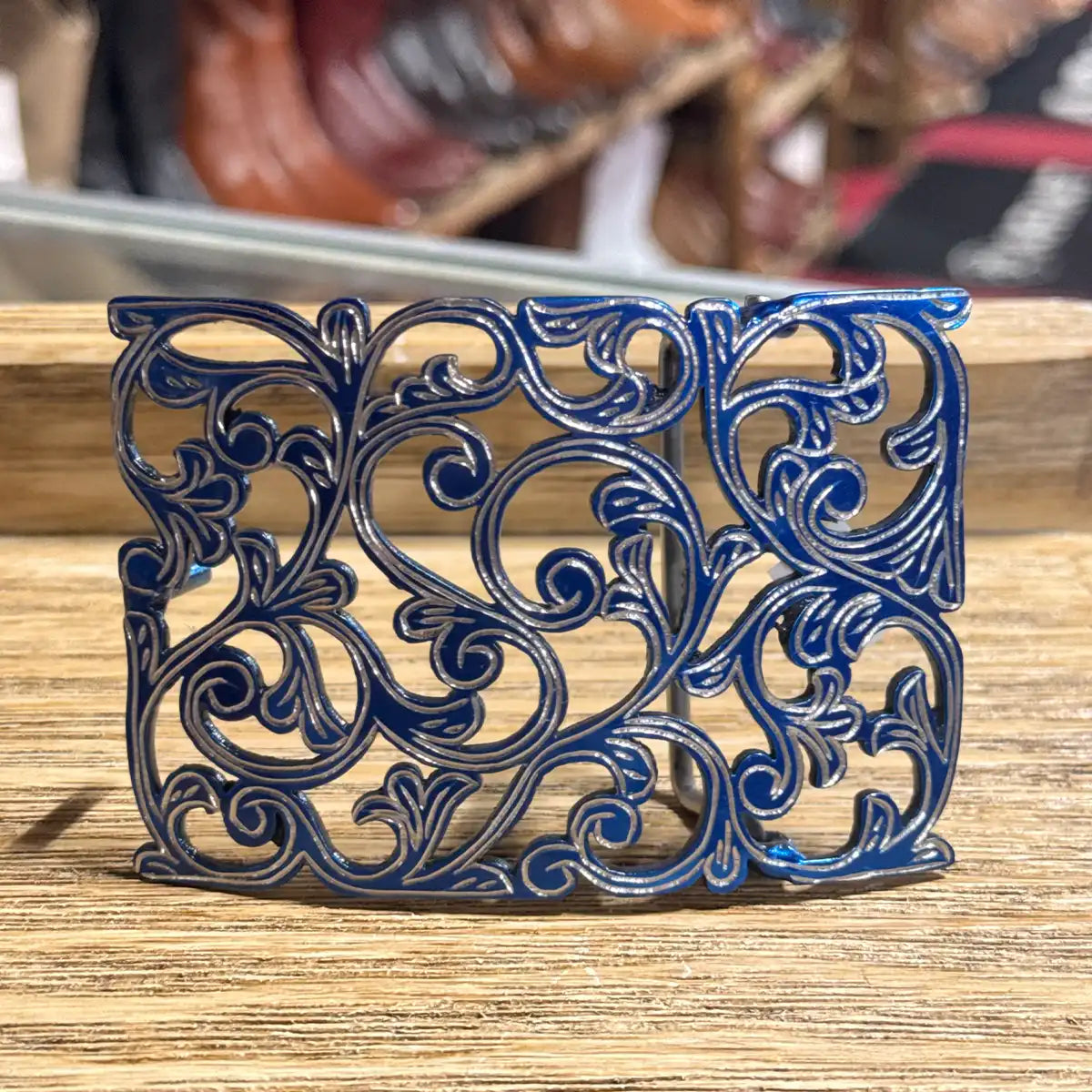 Front studio view of the 3.5" x 2.5" stainless steel cutout belt buckle showing the bright blue background finish and silver filigree scrollwork.