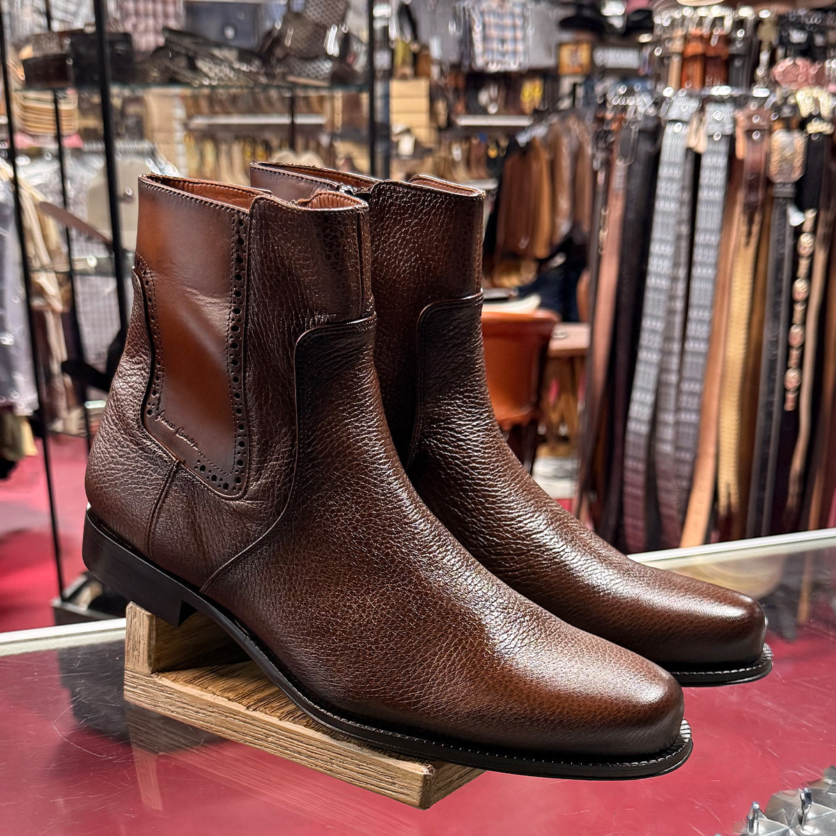 Pair of Cuadra men's brown leather boots on a wooden stand with a western wear store background.