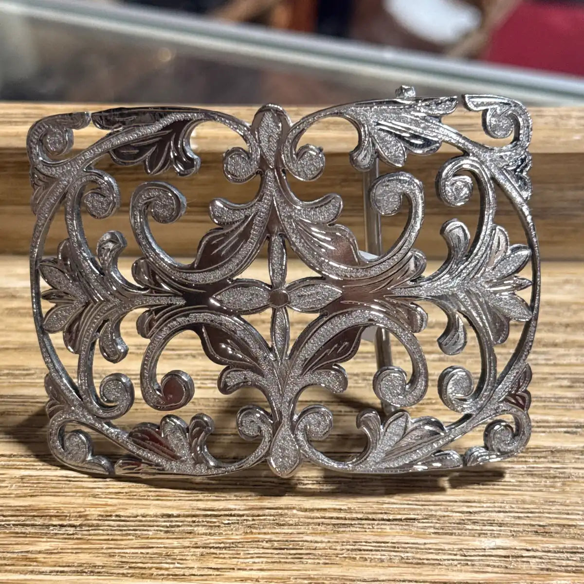 Stainless steel cutout Western belt buckle featuring a central four-petal floral cross motif surrounded by symmetrical filigree scrollwork.