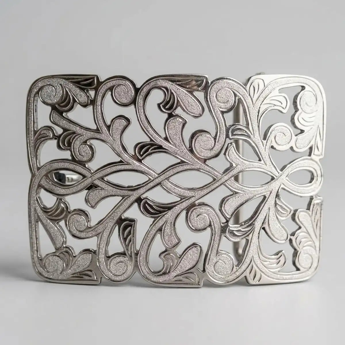 An ornate silver metal western belt buckle with an intricate filigree scrollwork design, shown on a neutral light gray background.