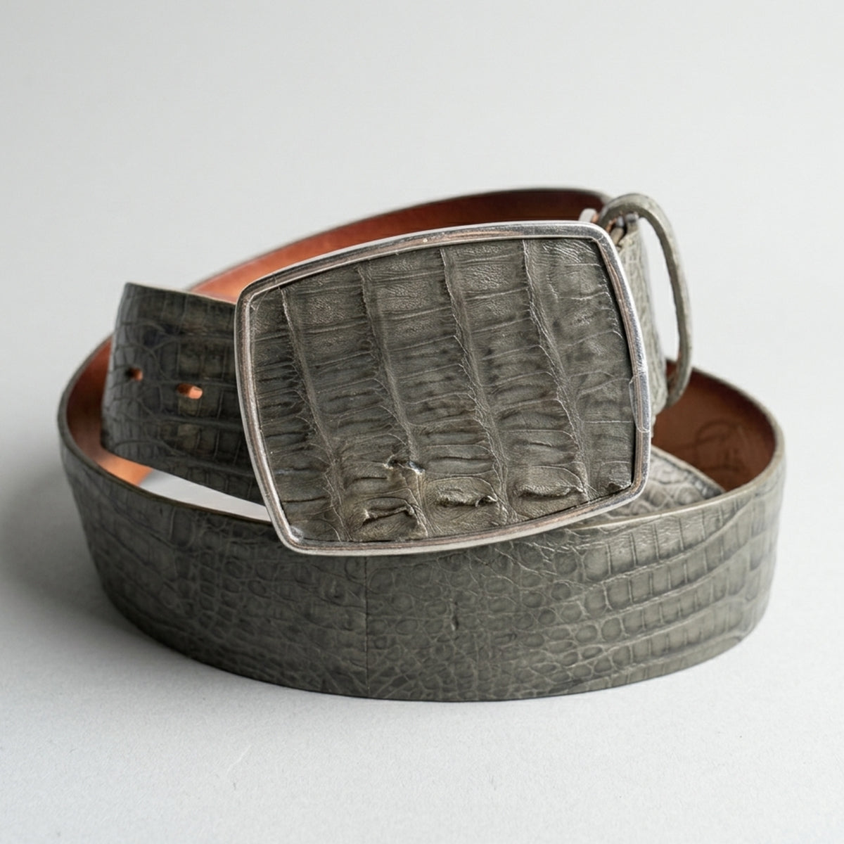 Gray crocodile belt with a matching buckle on a light gray background.
