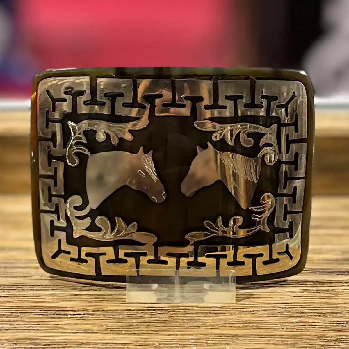 In-store counter display view of the handcrafted genuine bull horn belt western buckle showing the facing horses inlay on an acrylic stand.