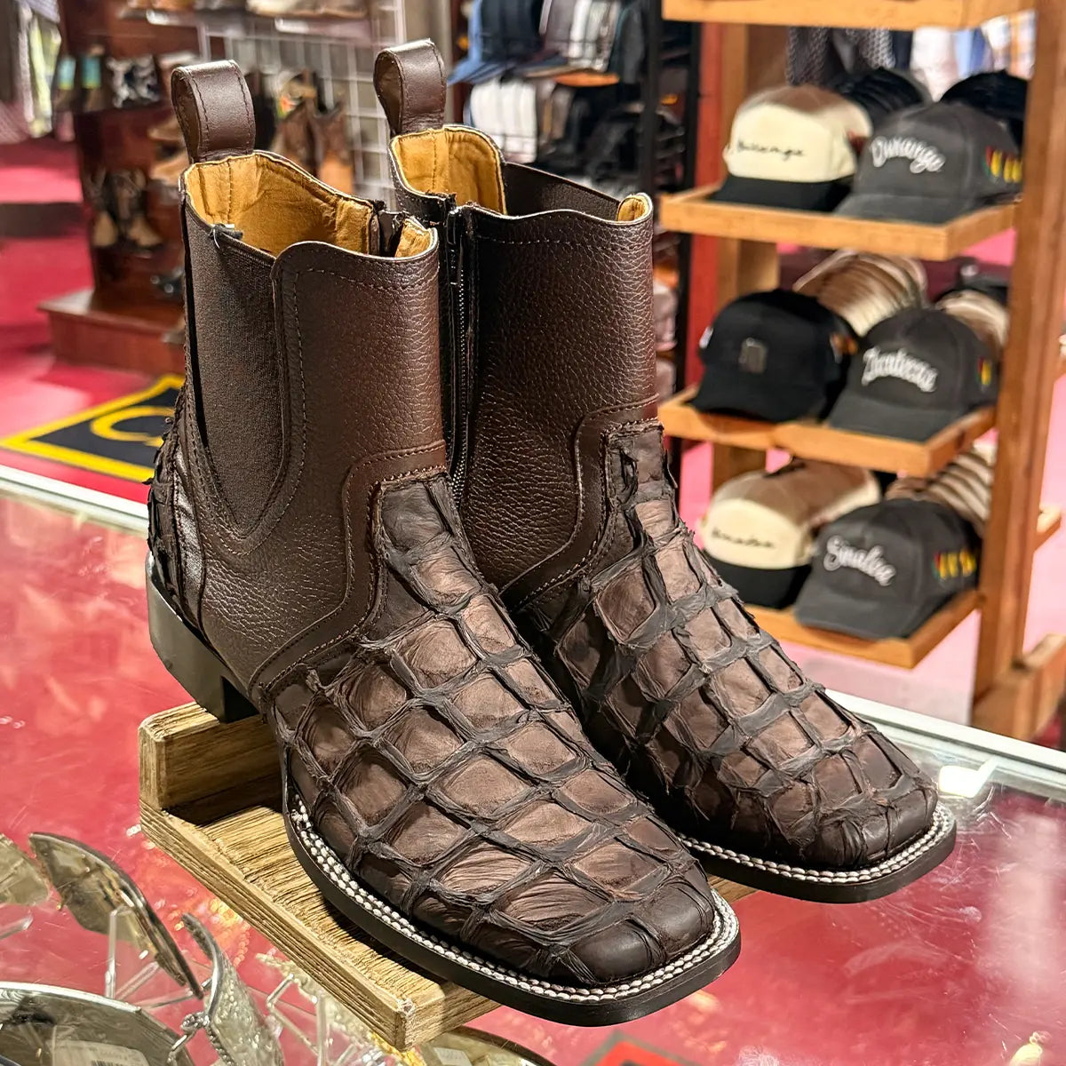 In-store display view of the Los Altos men's faded tobacco pirarucu Chelsea boots on a glass counter highlighting the detailed scale texture and square toe welt.