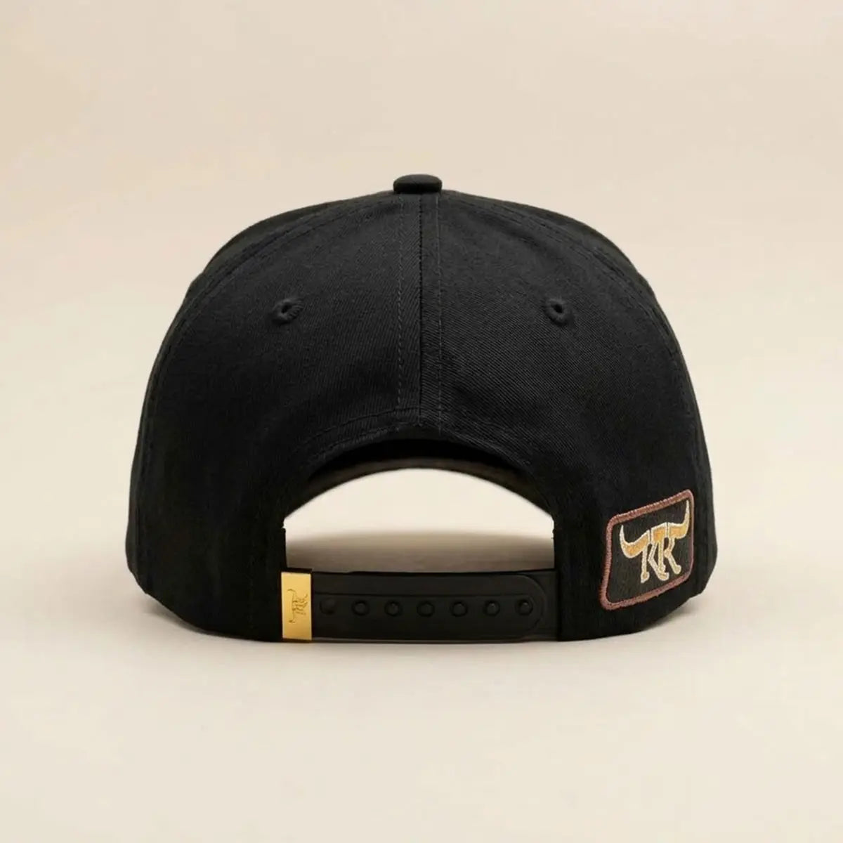 Back studio view of the King Ranch "Pantera" cap displaying the solid black fabric rear panels, temple longhorn patch, and gold clip snapback closure.