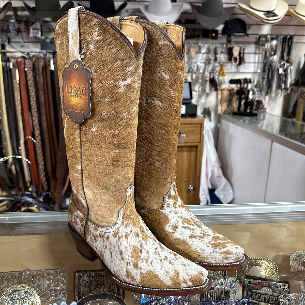 A pair of women's cowgirl boots with a brown and white cowhide pattern, displayed on a counter in a western store.