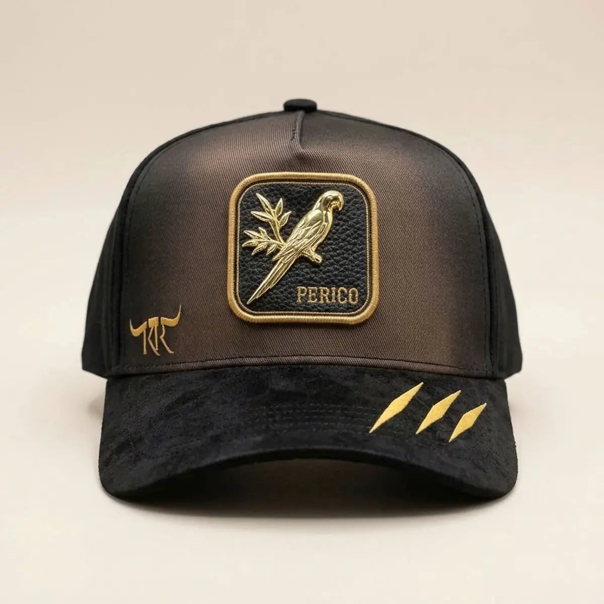 Front studio view of The King Ranch "Perico" brown and black snapback cap displaying the metallic gold parrot patch, suede visor, and claw accents.