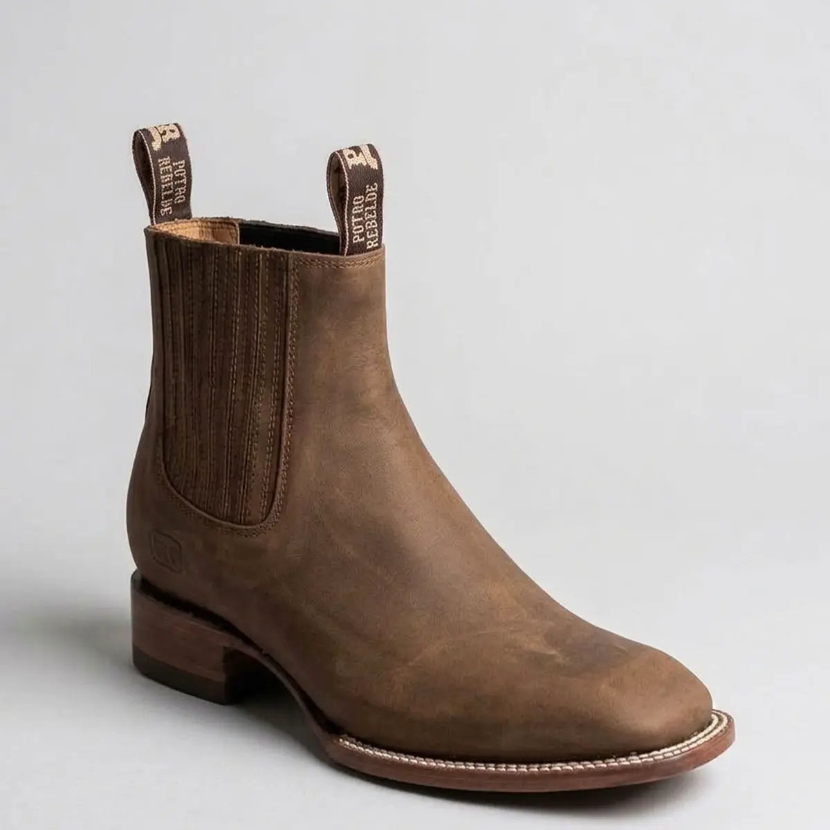 Studio profile view of the Potro Rebelde Men's topo brown leather Chelsea square toe boot showing the elastic side gore, pull tabs, and white welt stitching.