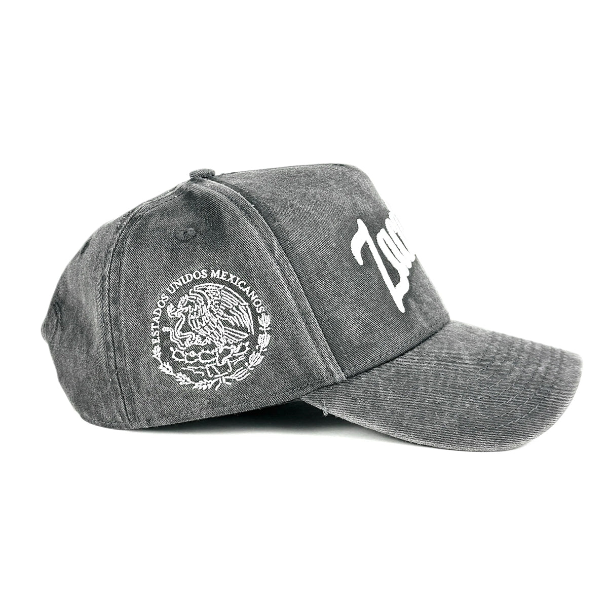A washed dark gray baseball cap featuring a white embroidered Mexican coat of arms on the side, shown against a plain white background.