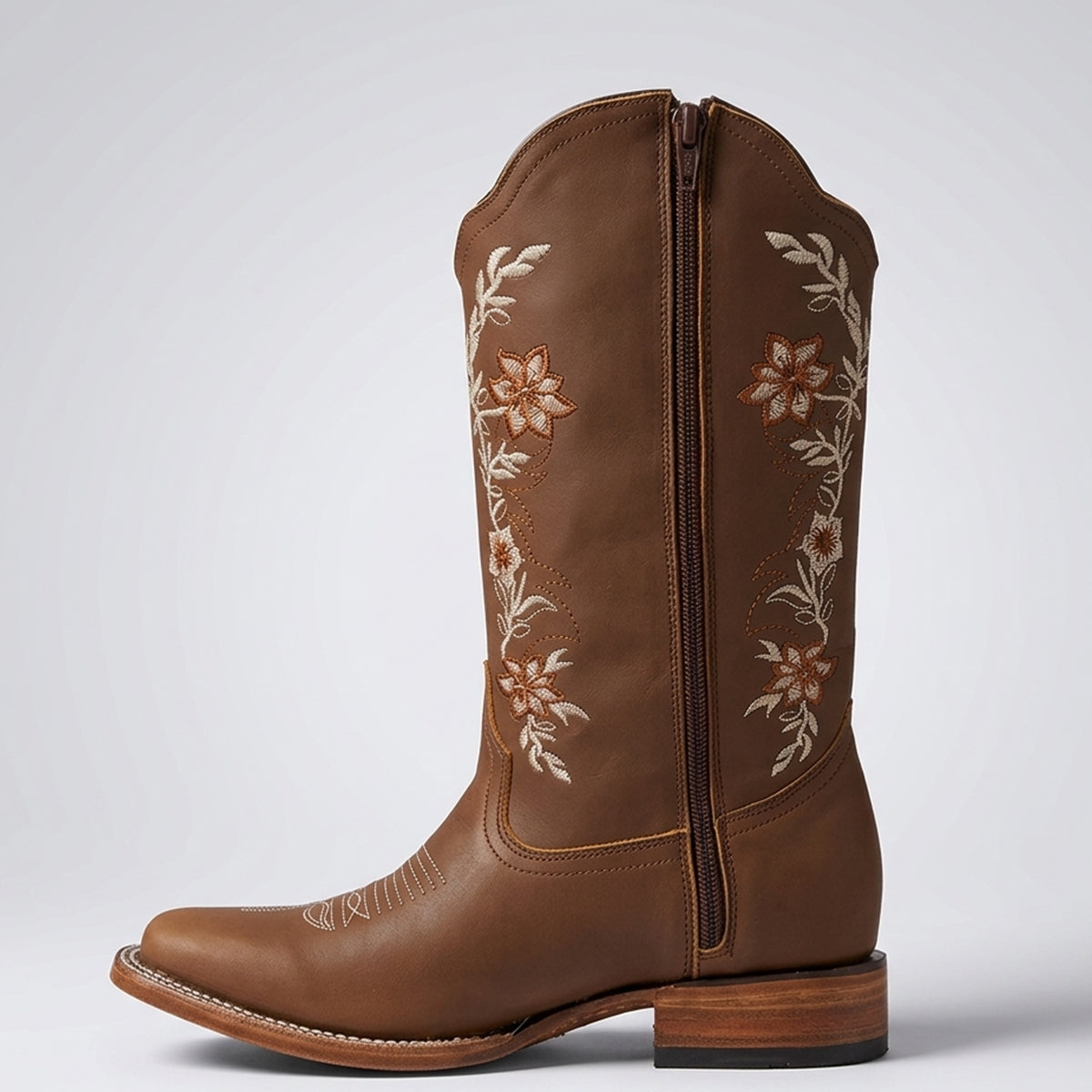 A women's brown leather cowboy boot with floral embroidery on the shaft, a square toe, and a side zipper, shown against a light gray background.