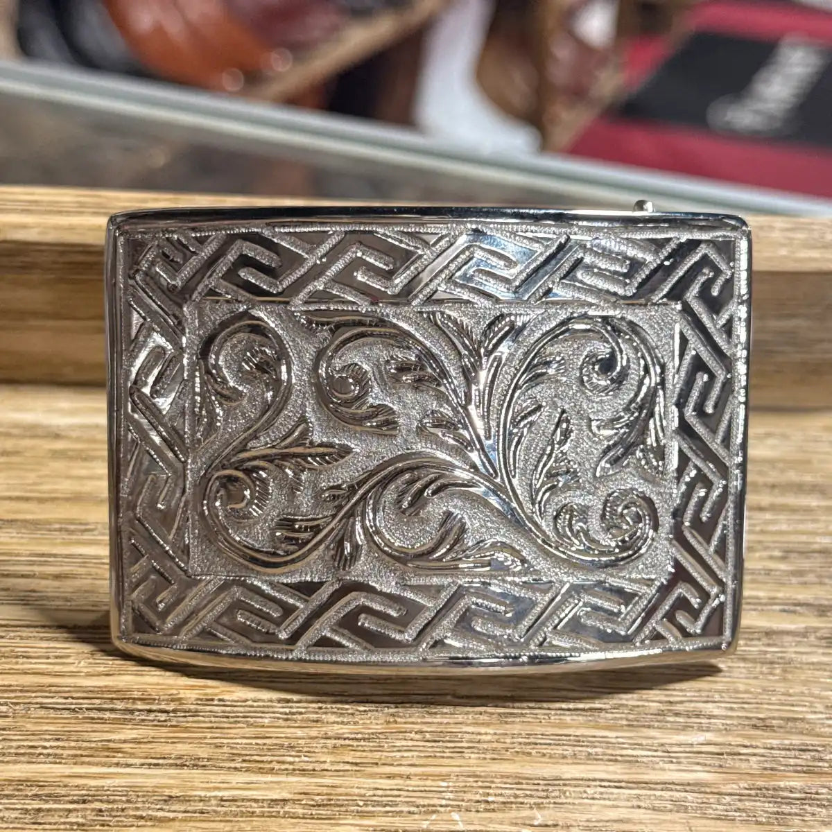 Stainless steel rectangular Western belt buckle featuring detailed floral scrollwork engraving, textured background, and geometric Greek key pattern border.