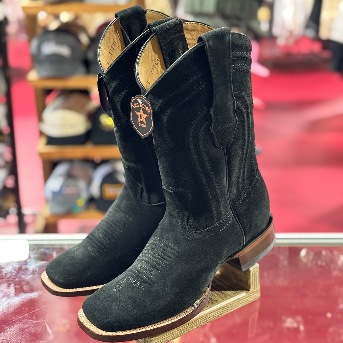 Los Altos men's lack suede square toe cowboy boots on a wooden stand with a blurred store background.
