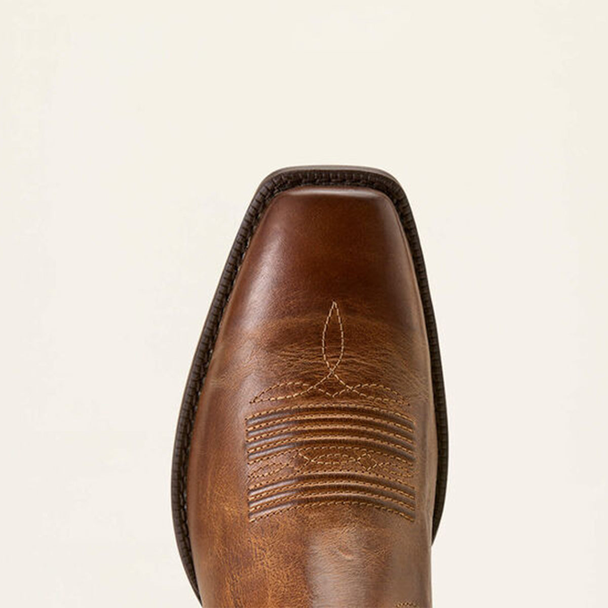 Close-up of a Ariat brown leather square toe on a beige background.