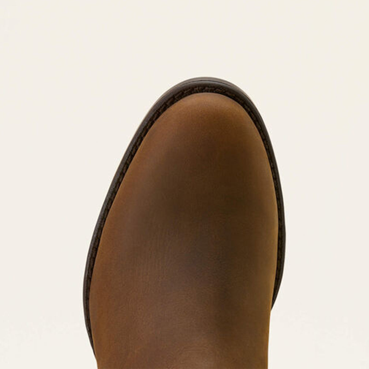 Close up of Ariat Sonoro brown leather boot toe on a beige background.