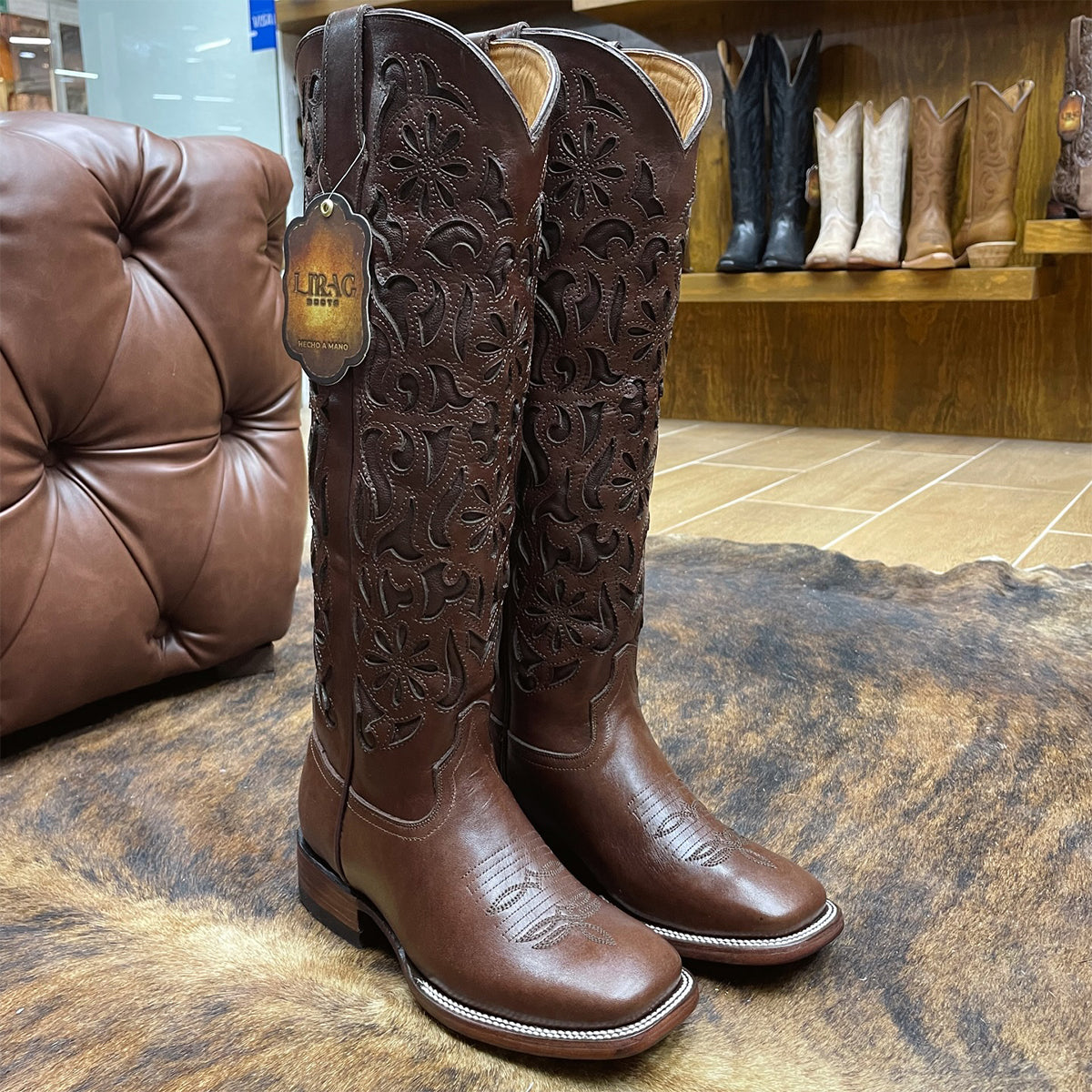 Pair of Lirac brown square toe cowgirl boots with intricate designs on a textured surface.