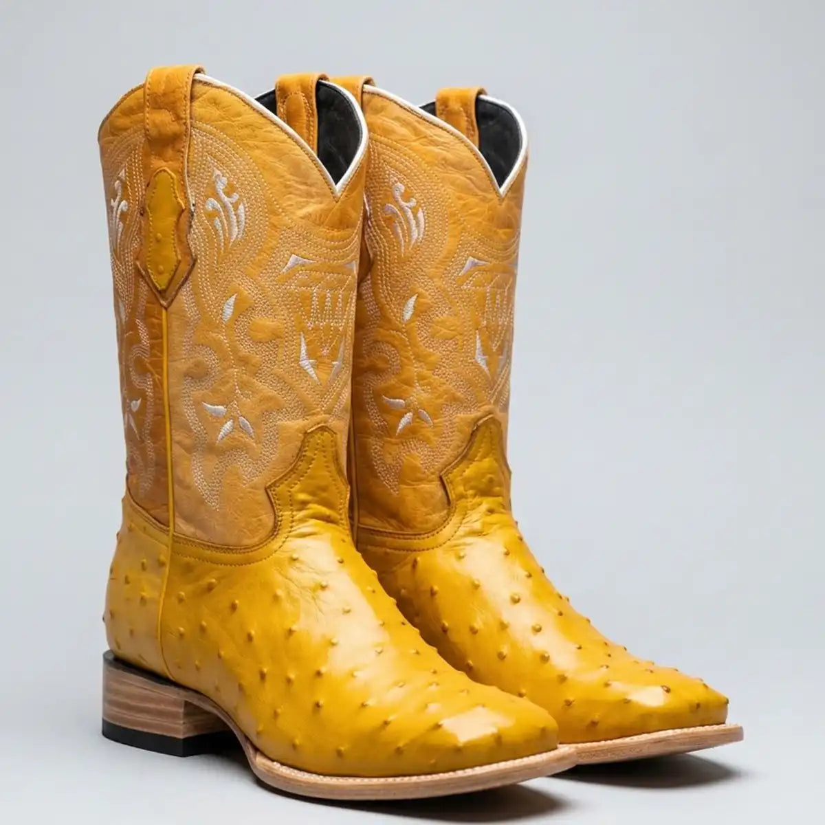 A pair of yellow ostrich print cowboy boots with white western embroidery on the shafts, shown against a neutral gray background.
