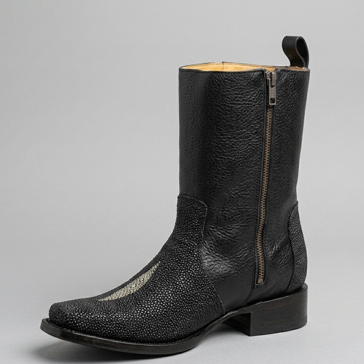 A single black leather western boot with a textured stingray print , a low block heel, and a side zipper, shown against a neutral gray background.